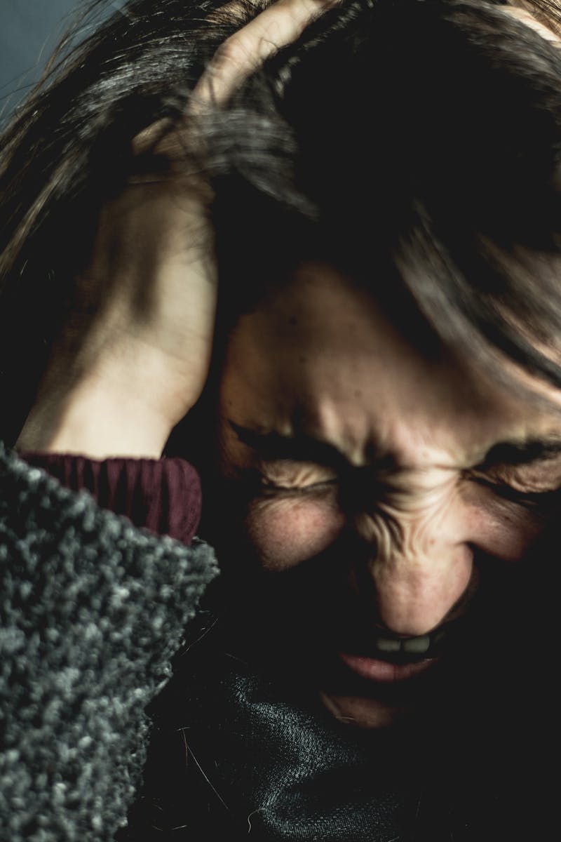 Close-up of a woman in distress with eyes closed and hands in hair, expressing anxiety.